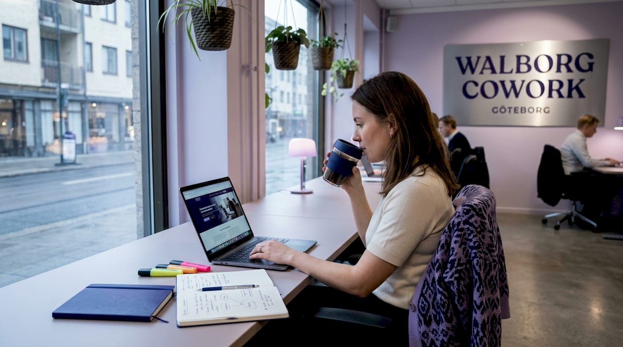 En person sitter och jobbar vid ett gemensamt skrivbord i en ljus och luftig coworkingmiljö.