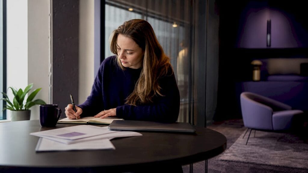 En kvinna sitter vid sitt skrivbord på kontoret och blickar ut över Göteborg genom fönstret.