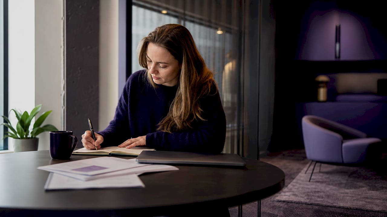En kvinna sitter vid sitt skrivbord på kontoret och blickar ut över Göteborg genom fönstret.