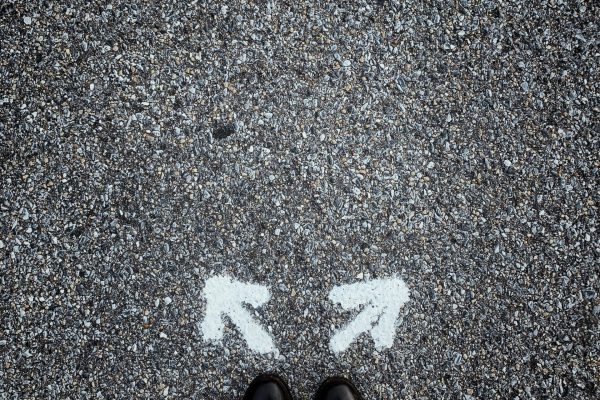 Two arrows painted on asphalt pointing in opposite directions in front of a pair of shoes